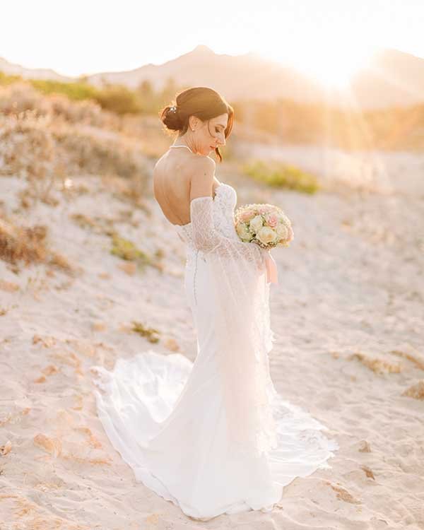 Sposa in spiaggia al tramonto con bouquet.