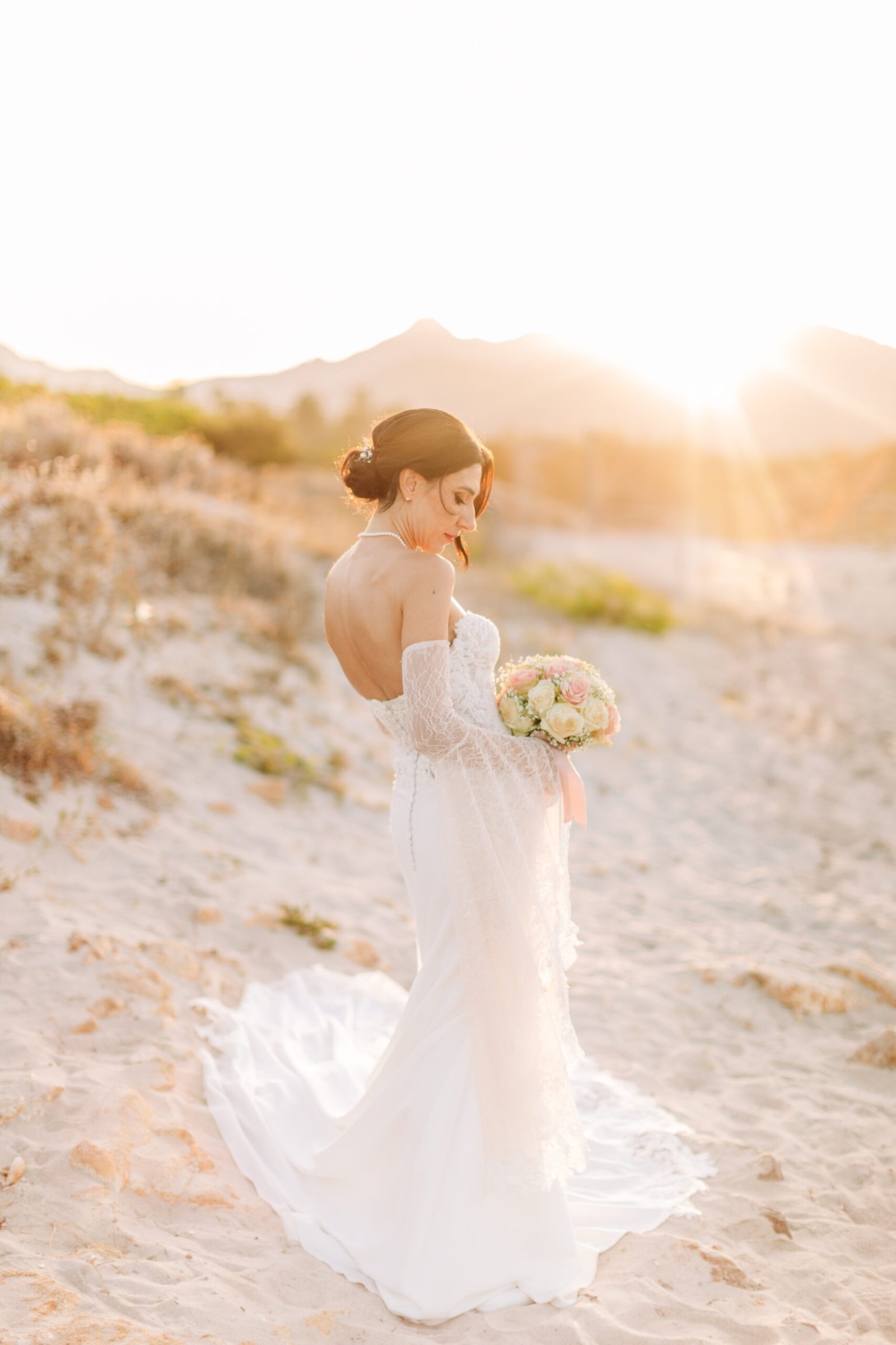 Sposa con bouquet su spiaggia al tramonto.