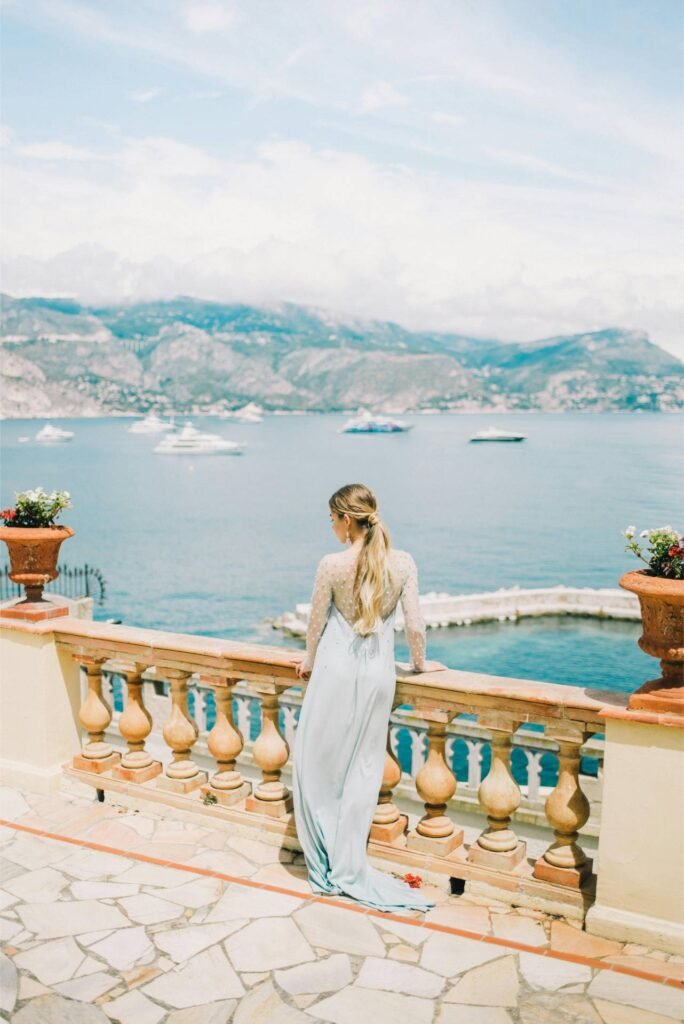 Donna in abito lungo guarda il mare e le montagne.